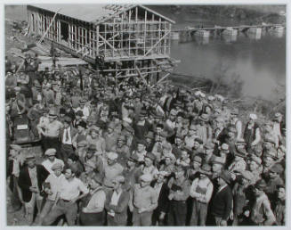 "A group showing some of the men working at Norris Dam site. In the rear can be seen the warehouse under construction and the foundation cribs for the heavy-duty bridge over the Clinch River.", 11/03/1933