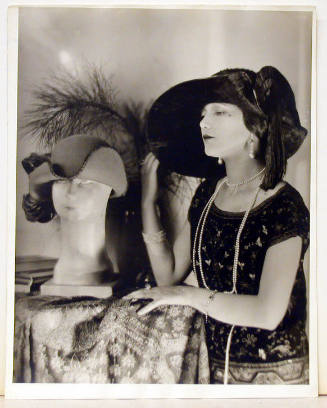 Untitled (Woman with pearls, wearing a hat, looking at a hat stand)